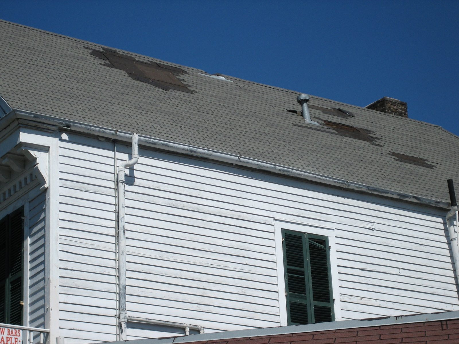 Aged asphalt shingle roof with multiple missing shingles exposing dark underlayment patches