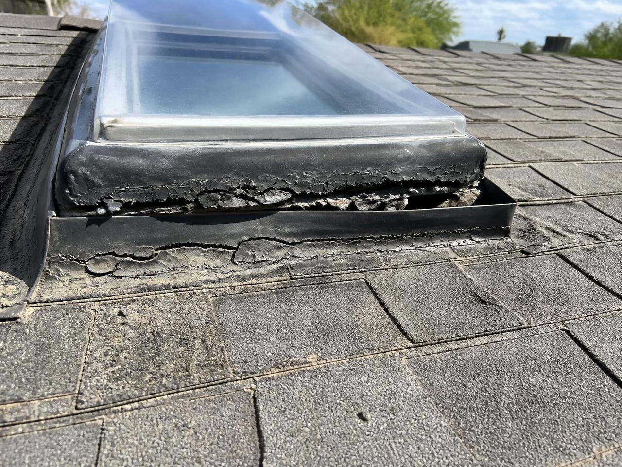 Close-up of a residential skylight on an asphalt shingle roof with cracked, delaminating black perimeter sealant and lifted flashing