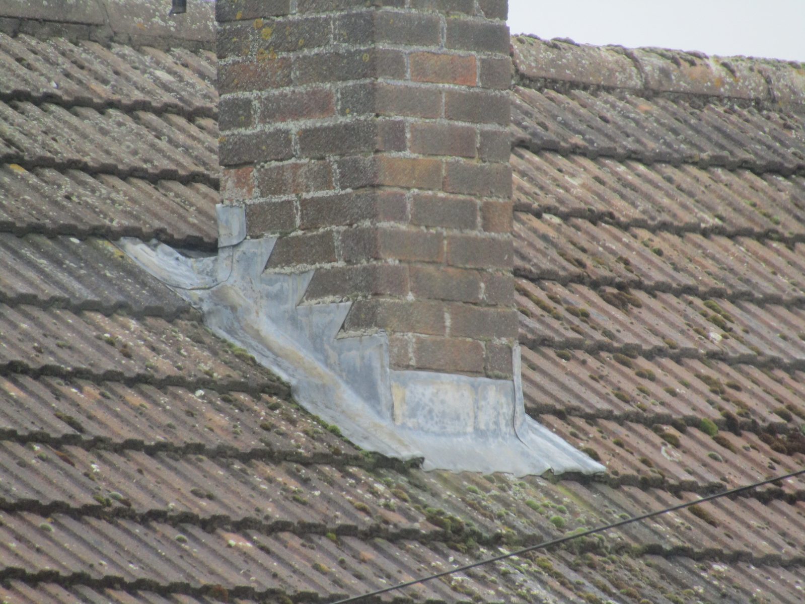 Brick chimney on a tile roof with lead step flashing lifted and separated from the tile course